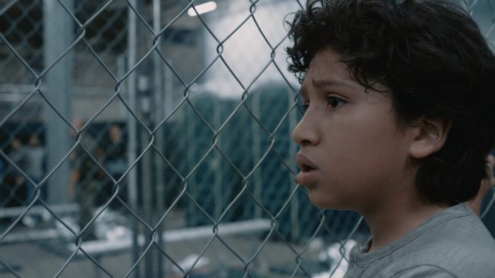 young child looking through metal fence
