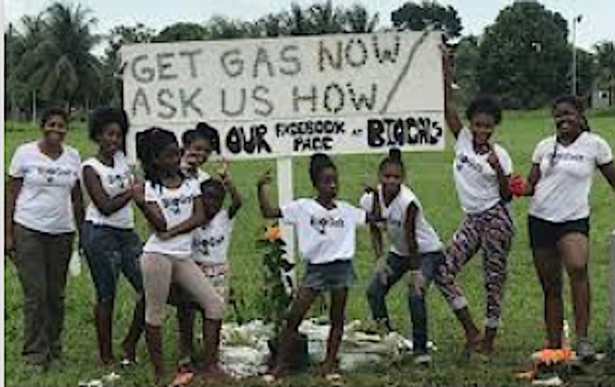 Photograph of women and girls in front of a sign that reads "get gas now, ask us how."