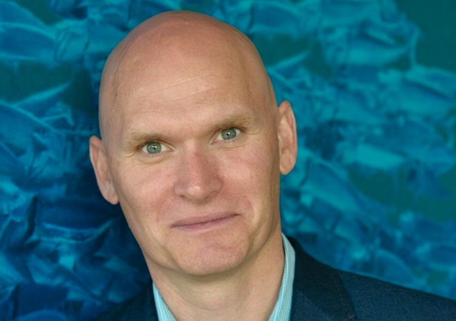 headshot of Anthony Doerr in a bright blue suit, with a blue shirt.