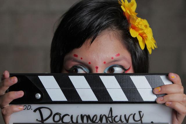 young girl's face with colorful makeup hiding behind movie marker