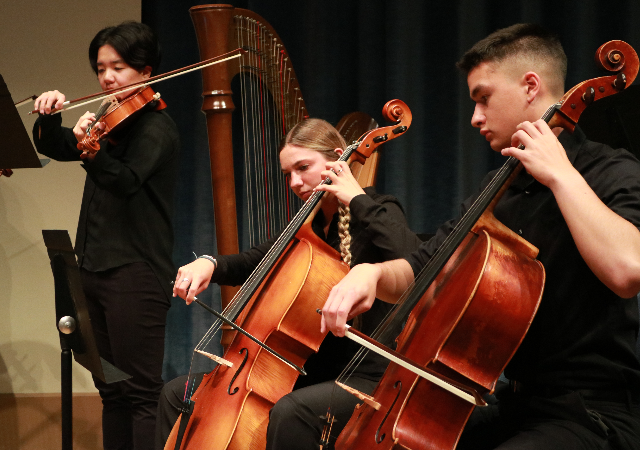 Two cellists and a violist performing on stage.