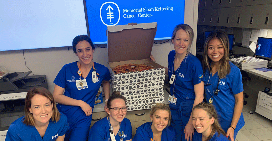 Smiling NYC nurses with a stack of pizzas