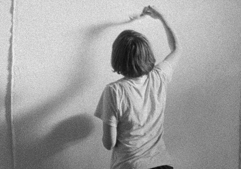 An artist stands in her studio, a paintbrush raised up to a blank canvas.