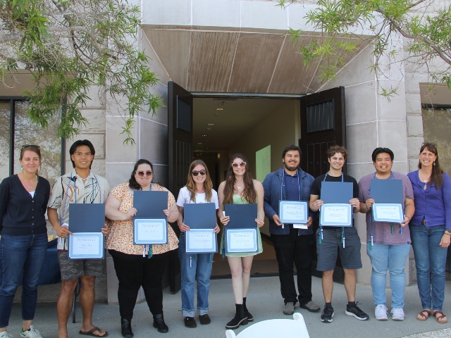 GIS graduates stand in front of a building holding their certificates