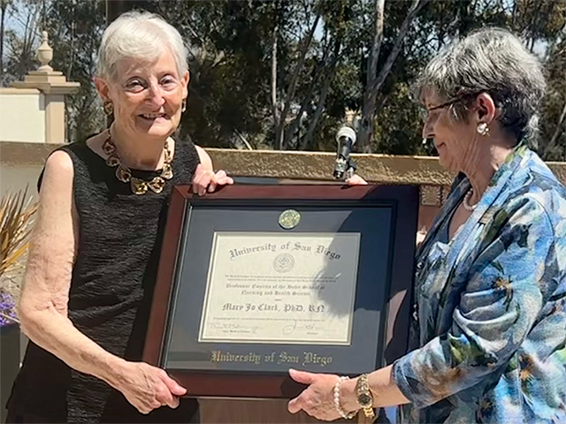 Dr. Mary Jo Clark, PhD, RN, receives a framed Professor Emerita certificate from Dean Jane M. Georges during an outdoor ceremony at the University of San Diego.