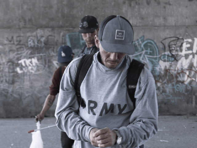 Three people walking past a cement wall