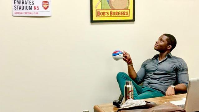 USD School of Business Assistant Professor of Economics Jason Campbell sits in his office chair looking up at his memorabilia of FC Barcelona soccer gear and Bob's Burgers poster