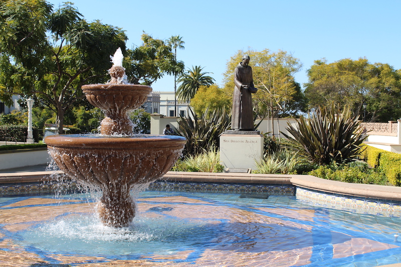 Water emerges from fountain on University of San Diego campus with a statue of a priest in the background