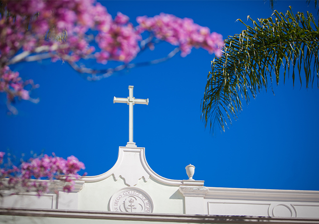 Image of a cross on a USD building with trees with pink blossoms in the foreground