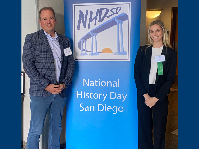 History major, Eleri Irons, stands next to History professor, David Miller, in front of a sign that reads "National History Day San Diego."