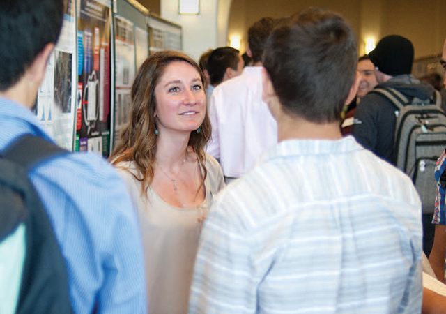 Female student presenting her poster to other students at Creative Collaborations.