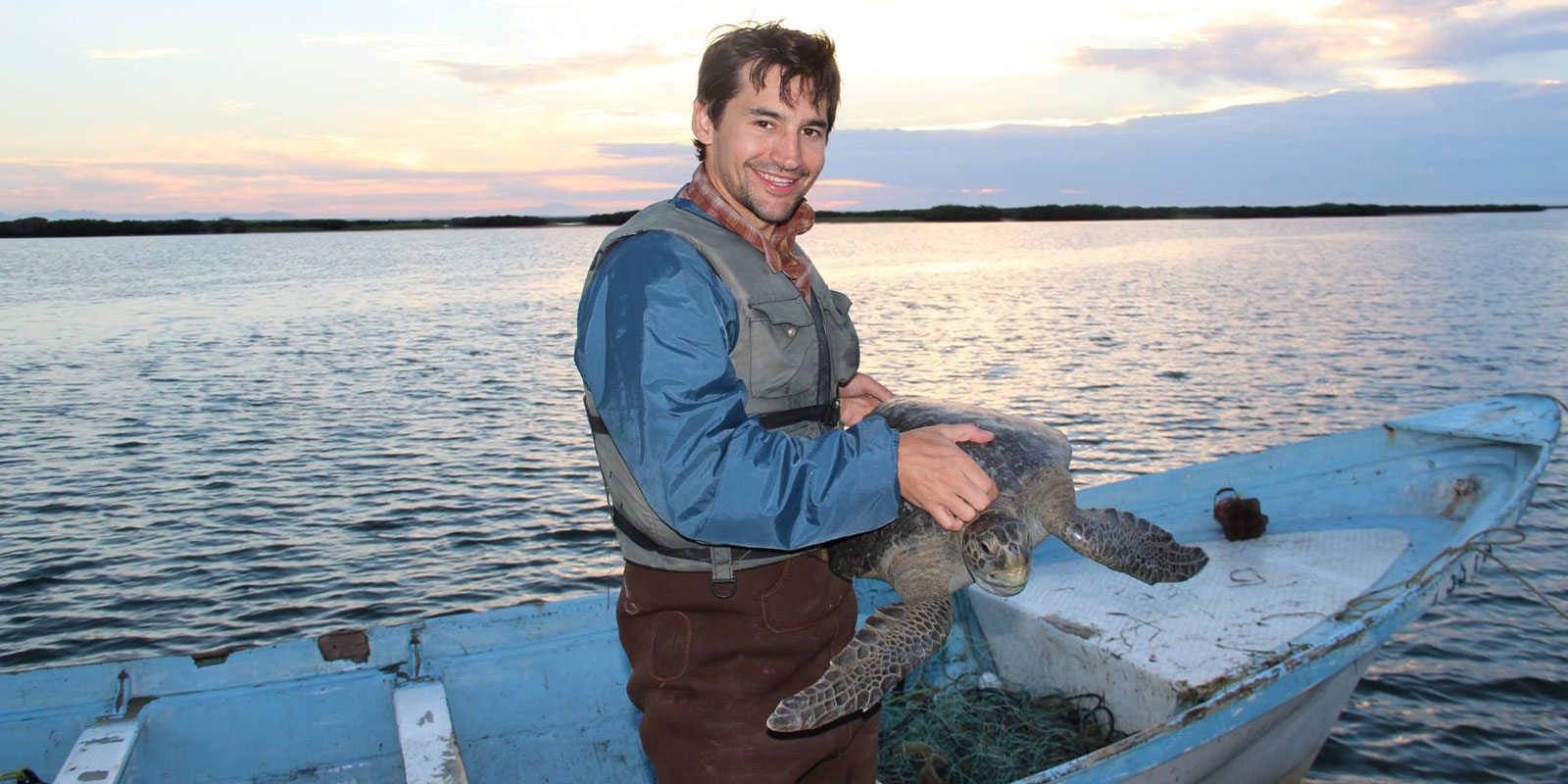 Travis Kemnitz holding a sea turtle on a small fishing boat