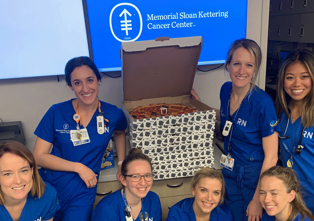 Smiling NYC nurses with a stack of pizzas