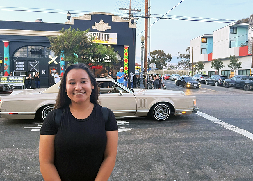 Amaya Ardilla posing on a street with a lowrider in the background