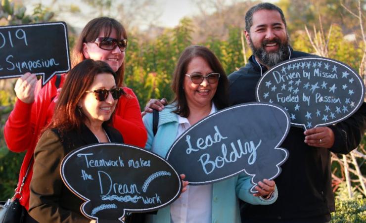 Four smiling people holding chalkboard signs with inspiring messages