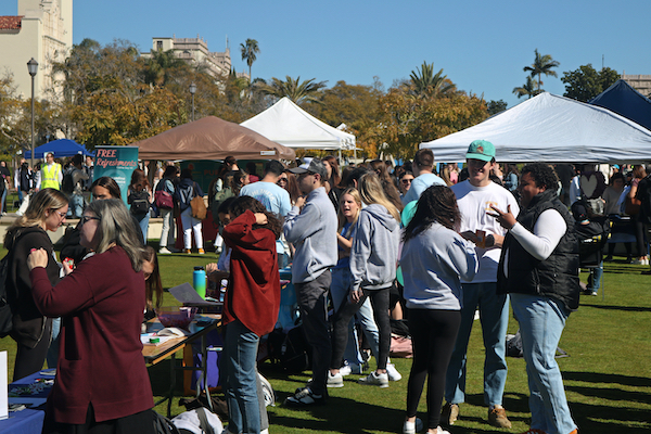 Students gathering and chatting at Alcala Bazaar tables located on the Paseo Lawn