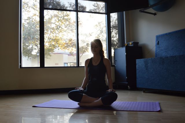 Student inside exercise studio sitting criss-cross during a meditation class
