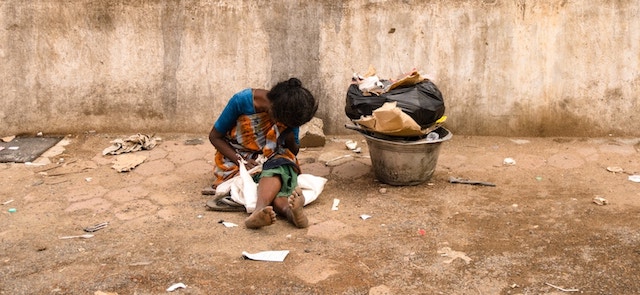 woman sitting on ground with no shoes near trash